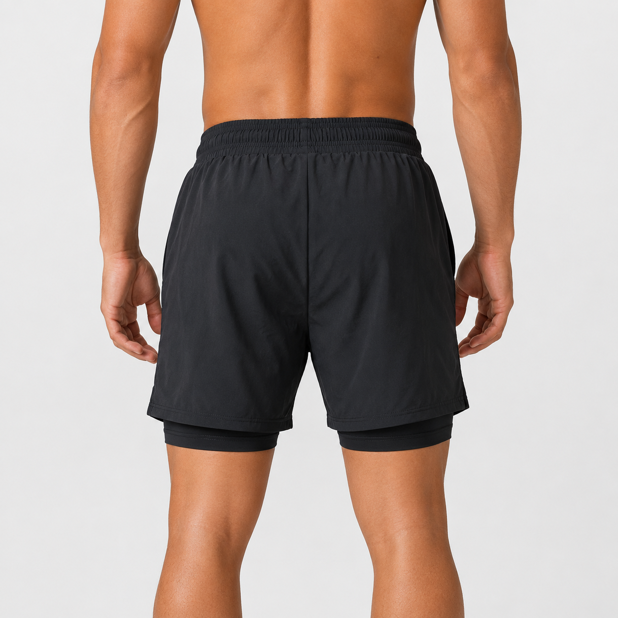 Pantaloneta deportiva negra para hombre con licra interna, pretina ajustable y logo Grama reflectivo, vista posterior.